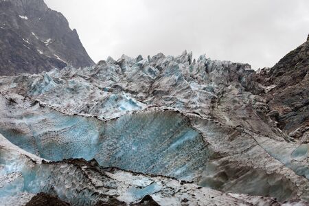 Glacier with deep crevasses covered with snow and ground in high rocky mountains at gray day. Caucasus Mountains. Georgia, region Svanetia.の写真素材