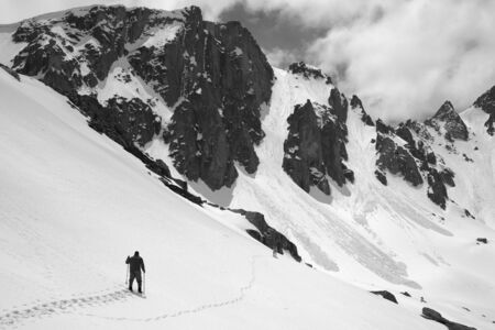 Snowy mountains with avalanche traces, sunlit cloudy sky, hiker with ski poles and dog on snowy slope at sunny day. Turkey, Kachkar Mountains, Pontic Mountains. Black and white toned landscape.の写真素材