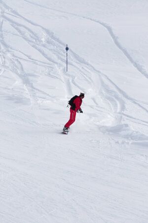 Snowboarder in red descends on snowy ski slope after snowfall at gray winter dayの写真素材