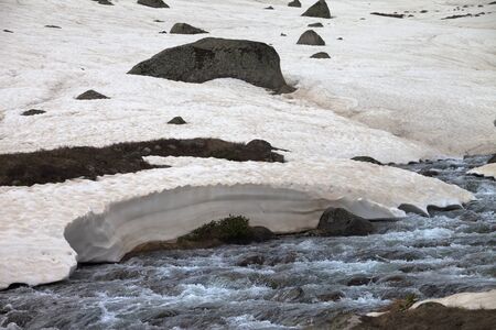 Clear mount river with snow bridges in high snowy mountains at spring eveningの写真素材