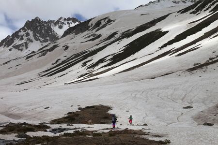 Silhouette of two hikers and dog on snow covered glacier with ground in spring snowy mountains at gray evening. Turkey, Kachkar Mountains (highest part of Pontic Mountains). Remote location. の写真素材