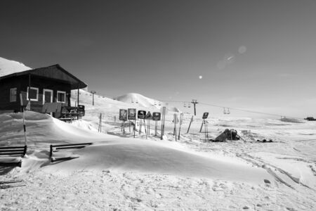 Black and white high snowy mountains, wooden rescue house, warning signs in snowdrift, chairlift and clear sky with sunbeam. Caucasus Mountains at sunny winter day. Georgia, region Gudauri. の写真素材