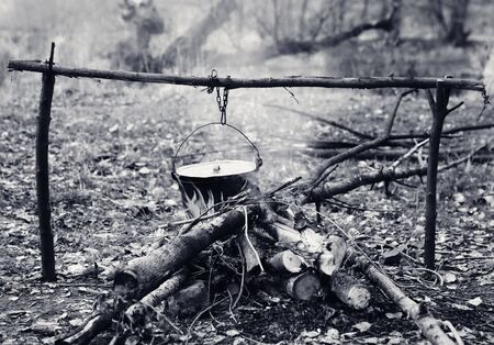 Cooking in old sooty cauldron on campfire at forest. Black and white retro toned image.の写真素材