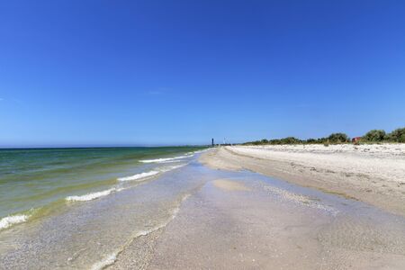 Clear sea with sand beach, blue sky and two lighthouses in distance at sun summer day. Wide angle view.の写真素材
