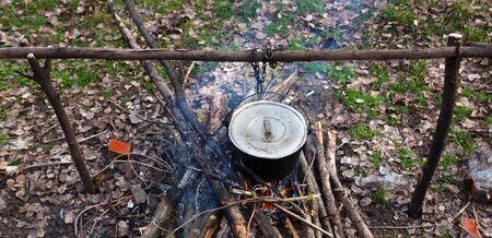 Cooking in old sooty cauldron on campfire at glade. Panoramic view.の写真素材