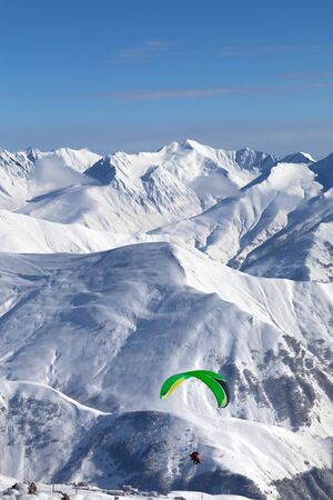 Paragliding at snowy mountains over ski resort at sunny cold day. Caucasus Mountains in winter. Georgia, region Gudauri.の写真素材
