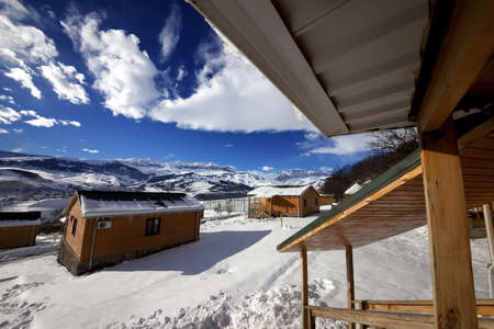 Courtyard with snow drift and small wooden houses at snowy winter mountains. Caucasus Mountains, Shahdagh, Azerbaijan. Wide angle view.のeditorial素材