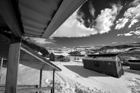 Courtyard with snow drift and small wooden houses at snowy winter mountains. Caucasus Mountains,...