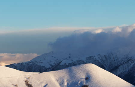 Snowy off-piste slope with tracks from skis and snowboards. High winter mountains in clouds at evening. Caucasus Mountains, Georgia, region Gudauri.の写真素材