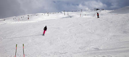 Ski poles, snowy ski slope with skiers in high mountains and cloudy sunlit sky at winter day. Ski...