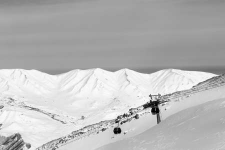 Snowy sunlit mountains and gondola lift at ski resort at sunny winter evening. Caucasus Mountains, Shahdagh, Azerbaijan. Black and white toned landscape.の写真素材
