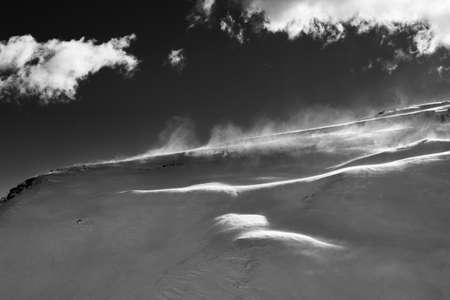 Off-piste slope during blizzard and sunlit sky with clouds in evening. Black and white toned landscape. High contrast.の写真素材