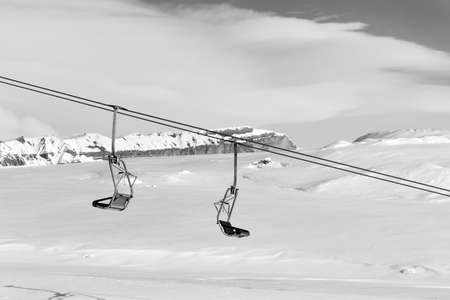 Snowy slope, chair-lift and sky with clouds at sun winter day. Caucasus Mountains, Shahdagh, Azerbaijan. Black and white toned landscape.の写真素材