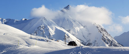 Panoramic view on snowy ski slope with trace from skis, snowboards and hotel on high mountains at winter evening. Caucasus Mountains. Georgia, region Gudauri.の写真素材