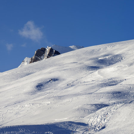Sunlit snowy ski slope with trace from skis and snowboards on high mountains at winter eveningの写真素材