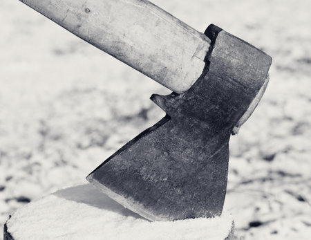 Axe in snowy log in winter forest. Black and white retro toned image. Close-up view.の写真素材