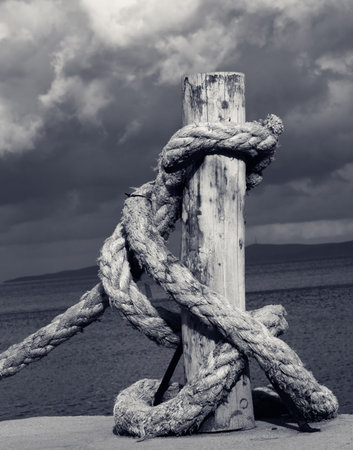 Rope on seafront, sea and beautiful cloudy sky in sun summer day. Black and white retro toned image. Close-up view.の写真素材