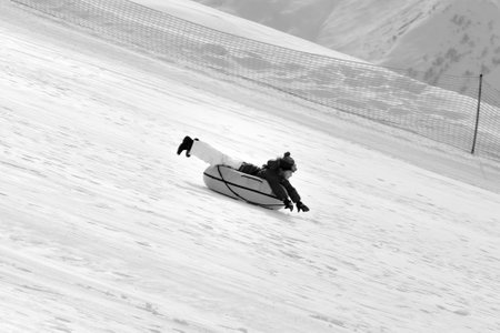 Young girl downhill on snow tube on ski resort at sun day in snowy mountains. Winter vacation. Black...