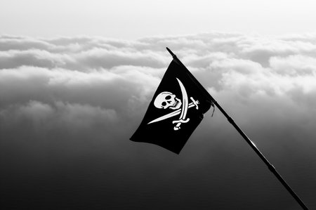 Jolly Roger - pirate flag on wind and sea in cloudy sky at background. Black and white toned image.の写真素材
