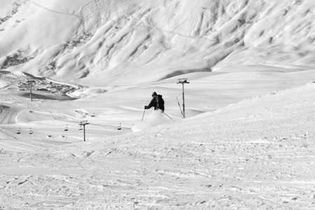 Skier descends on snowy ski slope in sun winter evening. Caucasus Mountains, Georgia, region Gudauri. Black and white toned image.の写真素材