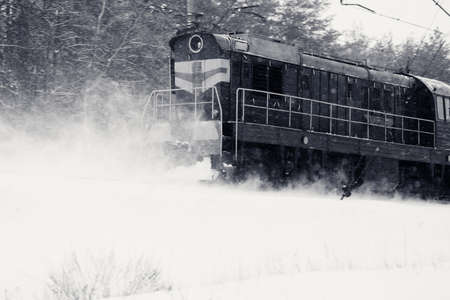 Ice covered train rides in snowstorm through snowy winter forest. Bad weather on railway. Black and white retro toned image.の写真素材