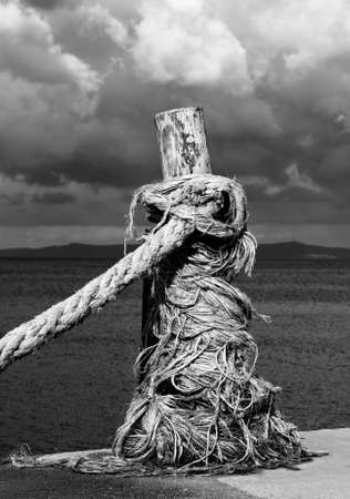 Rope on seafront, sea and cloudy sky in sunny summer day. Black and white toned landscape. High contrast. Close-up view.の写真素材