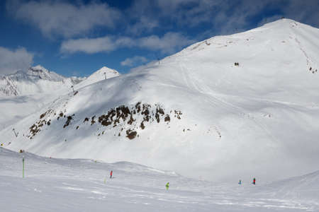 Skiers and snowboarders downhill on freeride trace and mountains with clouds at sun cold day. Caucasus Mountains in winter, Georgia, region Gudauri, mount Sadzele at background.の写真素材