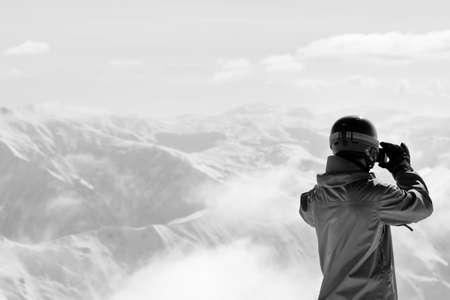 Snowboarder makes photo on camera and snow mountains in fog at background. Caucasus Mountains in...