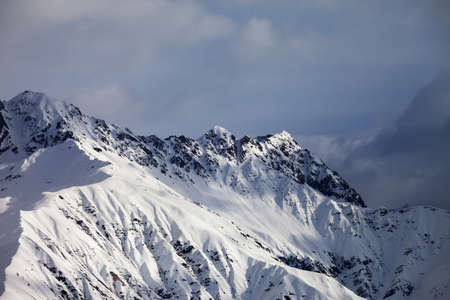 High snowy sunlight mountain and cloudy grey sky at winter evening. Caucasus Mountains. Svaneti region of Georgia.の写真素材