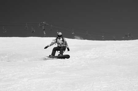 Snowboarder descends on snowy ski slope at winter mountains in sunny day. Old chairlift at background. Caucasus Mountains, region Dombay. Black and white toned image.の写真素材