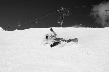 Snowboarder fall down with snow splashes on snowy off-piste ski slope and old chair lift at background. Caucasus Mountains in sunny winter day, region Dombay. Black and white toned image.の写真素材