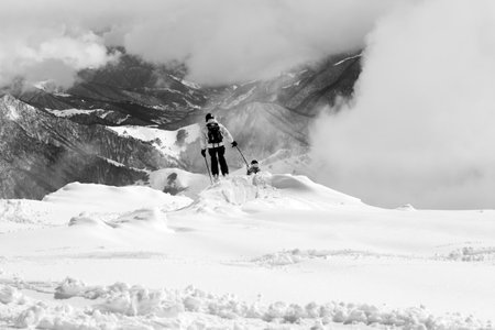 Freeriders on snowy off-piste slope and high mountains in mist. Caucasus Mountains, Georgia, region Gudauri at winter. Black and white toned image.の写真素材