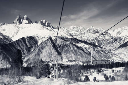 Chair-lift with skiers and snowy mountains at sunny winter day. Hatsvali, Svaneti region of Georgia. Caucasus Mountains, Mount Ushba at background. Black and white retro toned landscape.の写真素材