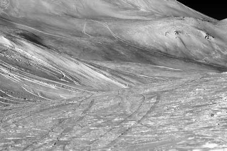 Snowy ski slope with traces from ski and snowboards at night. Caucasus Mountains in winter, Georgia, region Gudauri. Black and white toned landscape. High contrast.の写真素材