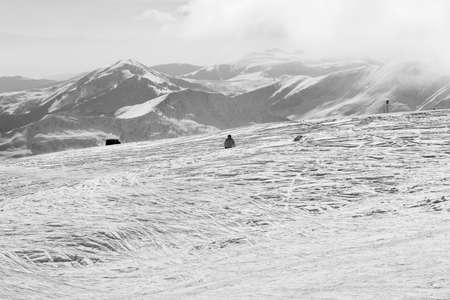 Skier downhill on snowy off-piste slope and mountains in haze at sun winter morning. Caucasus Mountains, Georgia, region Gudauri. Black and white toned image.の写真素材