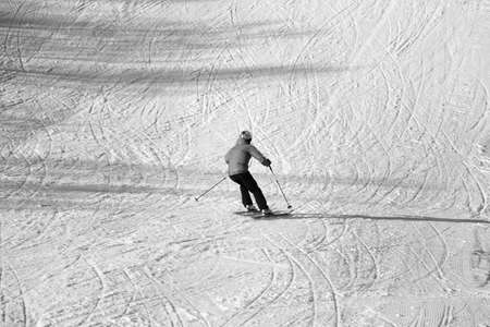 Skier descent on snowy ski slope with curves from skis at sunny winter day. Black and white toned image. High contrast.の写真素材