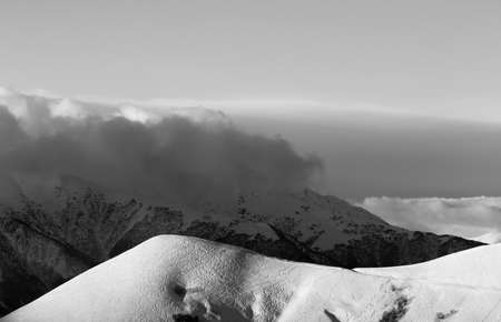 Snowy off-piste slope with tracks from skis and snowboards. High winter mountains in clouds at evening. Caucasus Mountains, Georgia, region Gudauri. Black and white toned landscape.の写真素材