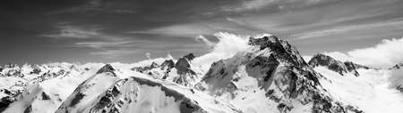 Black and white panorama of high snow-capped mountain peaks and beautiful sky with clouds at sun windy day. Caucasus Mountains in winter, region Dombay, mount Dombay-Ulgen.の写真素材