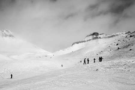 Skiers and snowboarders descent on snowy ski slope and overcast misty sky at day with bad weather before blizzard. Caucasus Mountains in winter, Georgia, region Gudauri. Black and whiteの写真素材