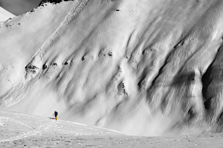 Skiers and off-piste slope with traces of skis, snowboards and avalanches. Caucasus Mountains in sunny winter day, Georgia, region Gudauri. Black and white toned landscape. High contrast.の写真素材