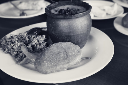 Lunch at Georgian cafe. Lobio of beans in clay pot, mchadi (cornbread), pickled appetizers: hot pepper and jonjoli (Staphylea colchica). Traditional Georgian cuisine. Black and white retro tonedの写真素材