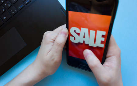 inscription sale on the phone screen.man holds a phone in his hand and sees the inscription sale.online shopping without leaving home during quarantine.black friday saleの写真素材