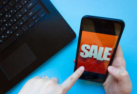 inscription sale on the phone screen.man holds a phone in his hand and sees the inscription sale.online shopping without leaving home during quarantine.black friday saleの写真素材
