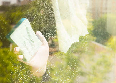 A woman polishing glass using a cleaning sponge and rubber gloves cleaning a window.the girl is...