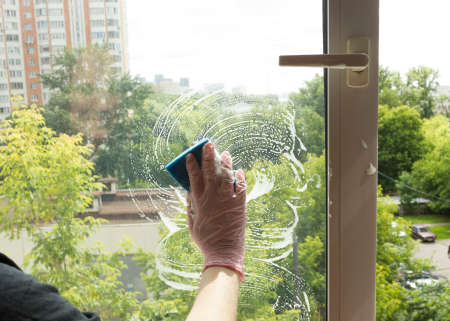 A woman polishing glass using a cleaning sponge and rubber gloves cleaning a window.the girl is cleaning the houseの写真素材