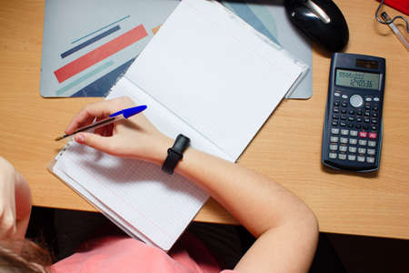 Girl Does math Homework in Her Living Room. Shes Sitting at Her Desk Writes with a Pen in Her...