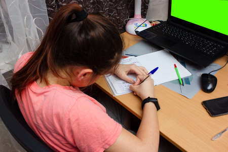 Smart Little Girl Does Homework in Her Living Room. Shes Sitting at Her Desk Writes with a Pen in...
