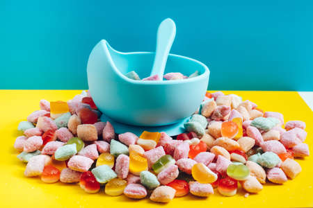 Childrens tableware silicone bowl with spoon. Serving baby food, kid dishware.blue silicone bowl and spoon are in a heap of sweets and marmalade. bright, colorful photoの写真素材