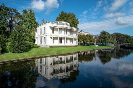 Vicorian white house reflection on a calm canal water under a very sunny and blue sky day at The Hague, Netherlandsの写真素材