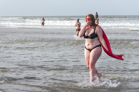 SCHEVENINGEN, 1 January 2018 - Strong girl disguised with a mask and cape getting to the beach after having accomplished the new year dive in a frozen North Sea water at Unox new year diveのeditorial素材